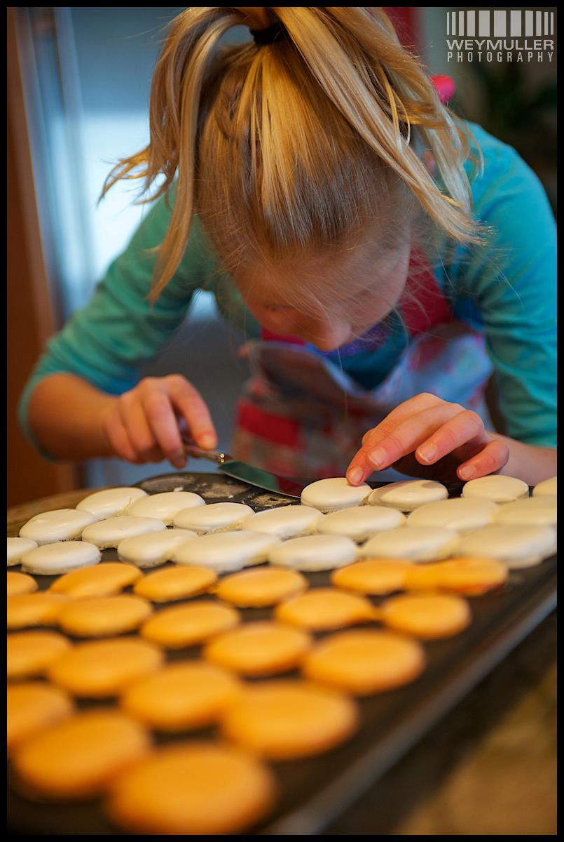 Young Hannah carefully arranging trays of orange and white macarons. Photo by Weymuller Photography.