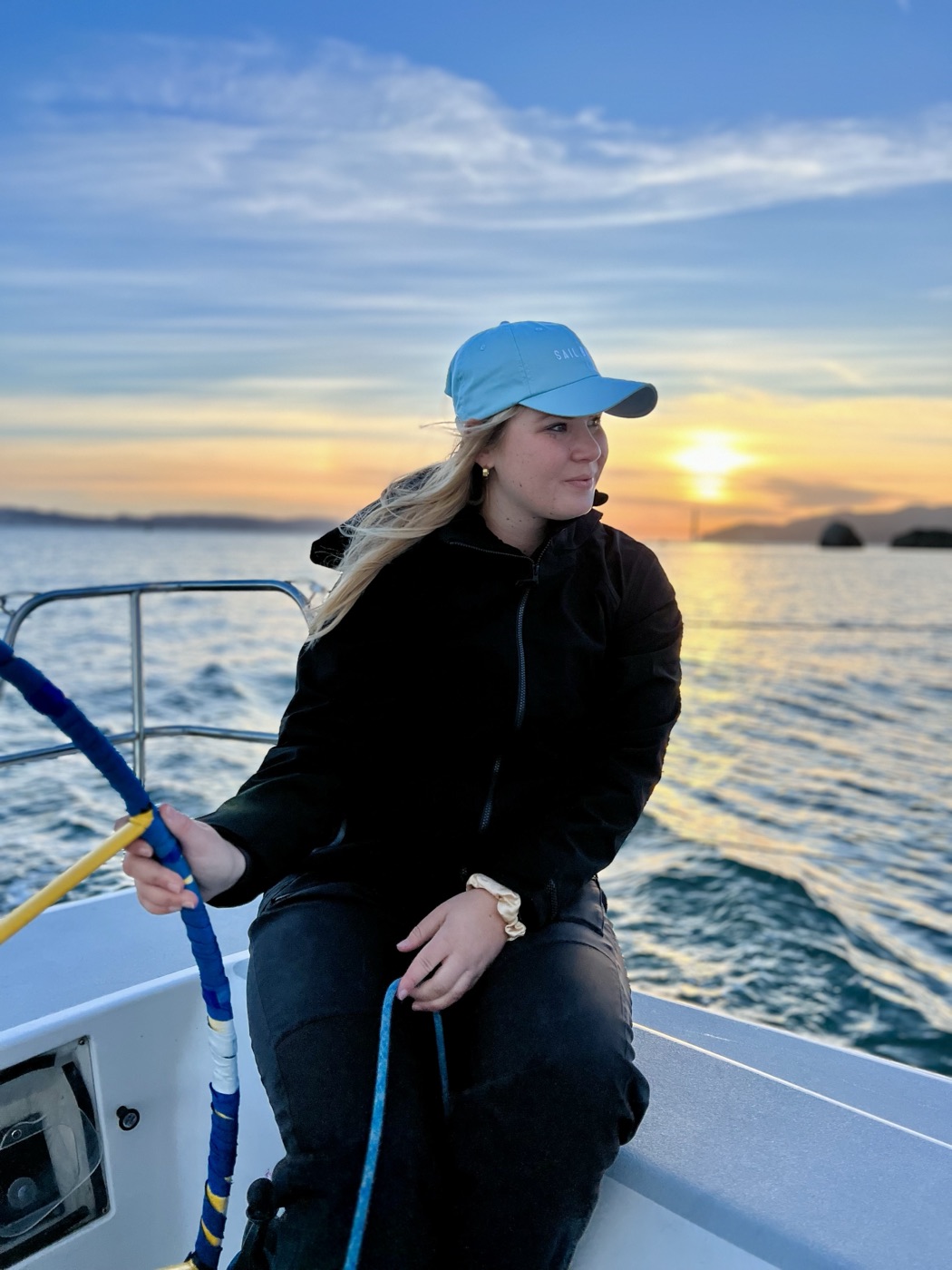On a sailboat at sunset, holding a line, looking out across calm water